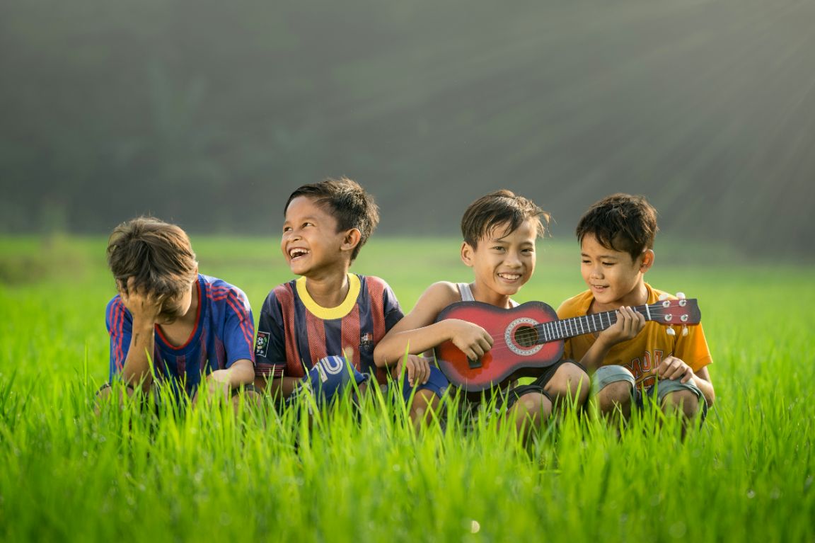 four children playing a guitar and playing in high grass